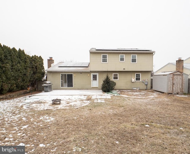 snow covered back of property featuring a shed, an outdoor fire pit, and solar panels