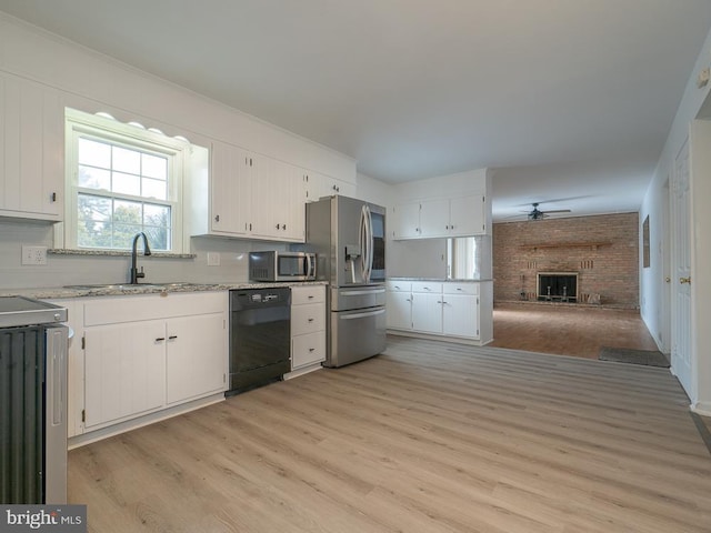 kitchen featuring light hardwood / wood-style flooring, a brick fireplace, appliances with stainless steel finishes, white cabinets, and sink