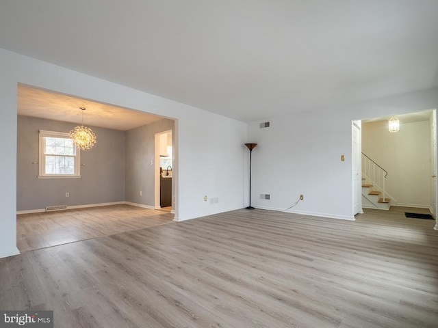 unfurnished living room featuring an inviting chandelier and light hardwood / wood-style flooring