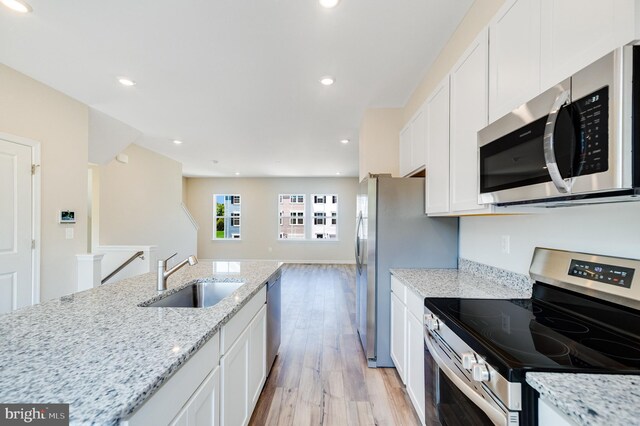 kitchen featuring sink, white cabinetry, light hardwood / wood-style flooring, stainless steel appliances, and light stone counters