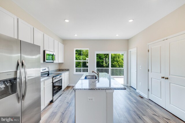 kitchen featuring appliances with stainless steel finishes, a kitchen island with sink, white cabinets, and light stone countertops