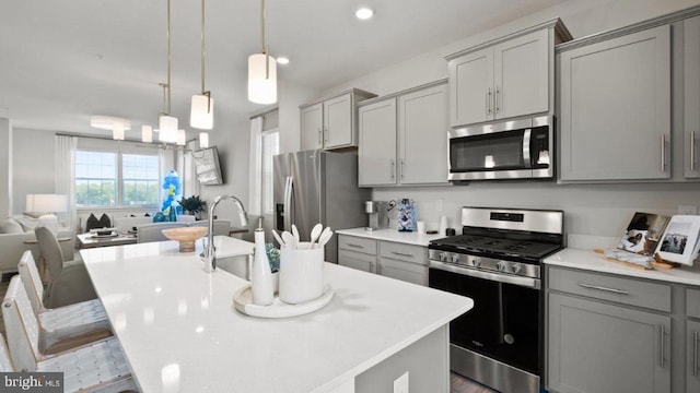 kitchen featuring decorative light fixtures, gray cabinets, stainless steel appliances, and an island with sink