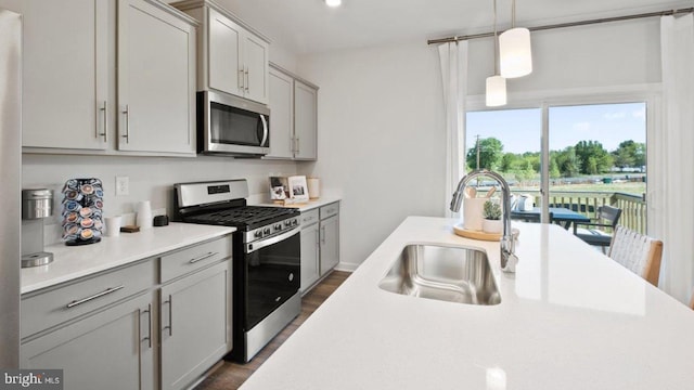 kitchen with appliances with stainless steel finishes, gray cabinetry, dark wood-type flooring, hanging light fixtures, and sink