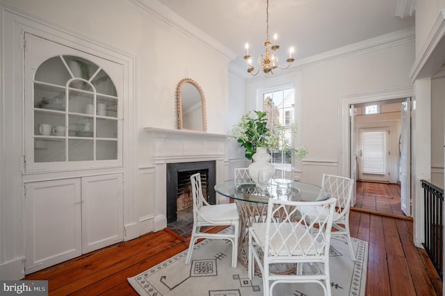 dining room featuring a notable chandelier, dark wood-style floors, a fireplace with flush hearth, and crown molding