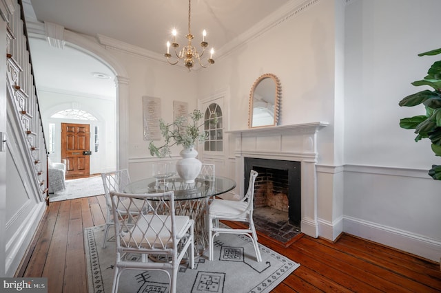 dining space featuring hardwood / wood-style flooring, a wainscoted wall, a fireplace, ornamental molding, and an inviting chandelier