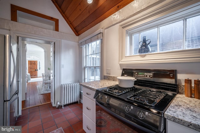 kitchen featuring black range with gas cooktop, radiator, freestanding refrigerator, vaulted ceiling, and dark tile patterned floors