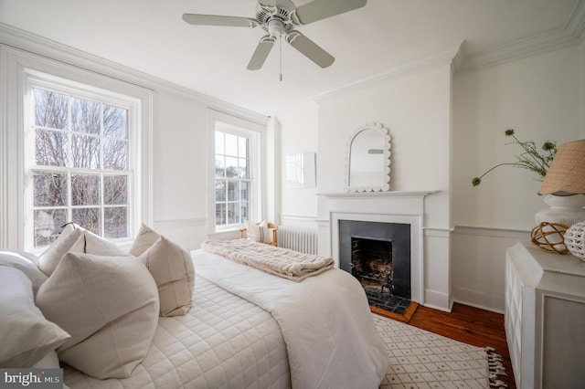 bedroom featuring a fireplace, crown molding, radiator heating unit, a ceiling fan, and wood finished floors