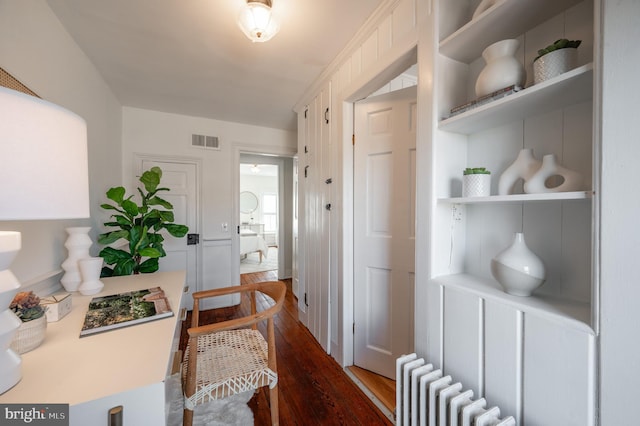 hallway featuring dark wood-style flooring, built in features, visible vents, and radiator