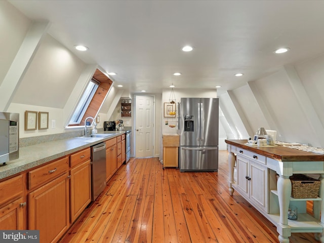 kitchen with sink, kitchen peninsula, stainless steel appliances, vaulted ceiling with skylight, and light hardwood / wood-style floors