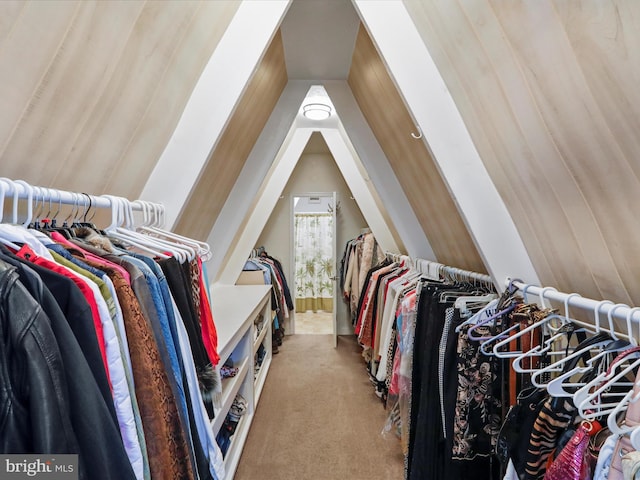 walk in closet with vaulted ceiling and light colored carpet