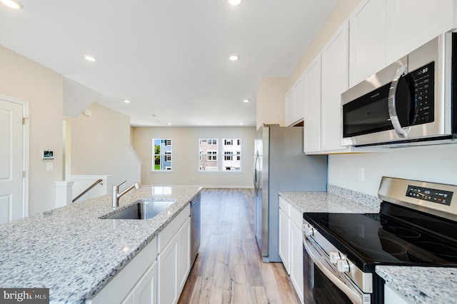 kitchen with white cabinetry, stainless steel appliances, light wood-type flooring, light stone counters, and sink