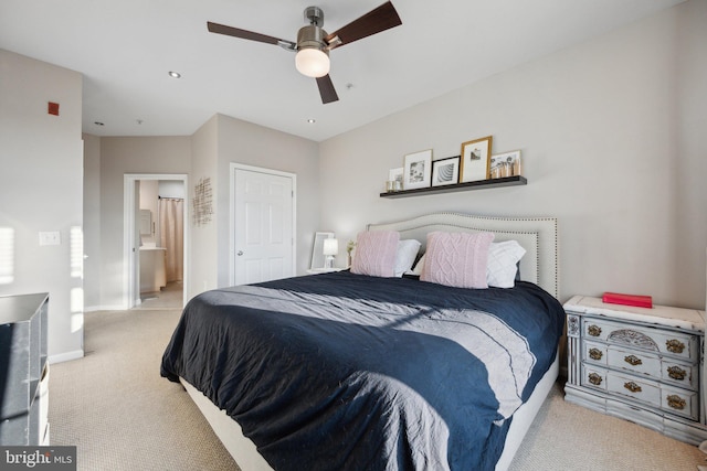 bedroom with ensuite bathroom, light colored carpet, and ceiling fan