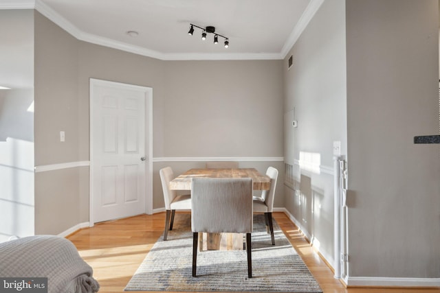 dining room featuring rail lighting, crown molding, and light hardwood / wood-style flooring