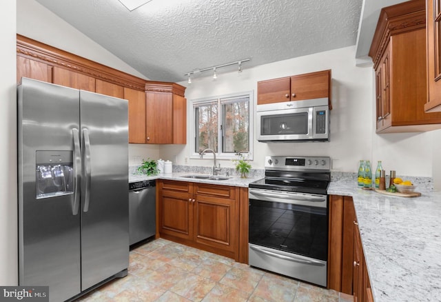 kitchen featuring vaulted ceiling, light stone countertops, stainless steel appliances, and sink