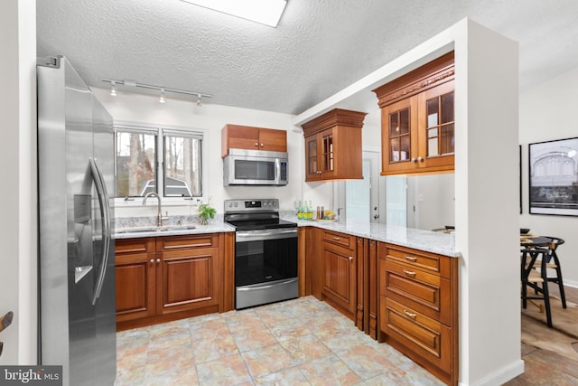 kitchen featuring a textured ceiling, appliances with stainless steel finishes, light stone counters, and sink