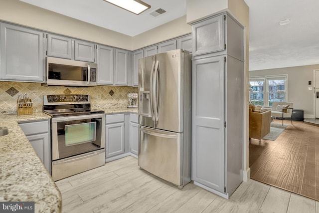 kitchen with light stone counters, tasteful backsplash, gray cabinetry, and appliances with stainless steel finishes