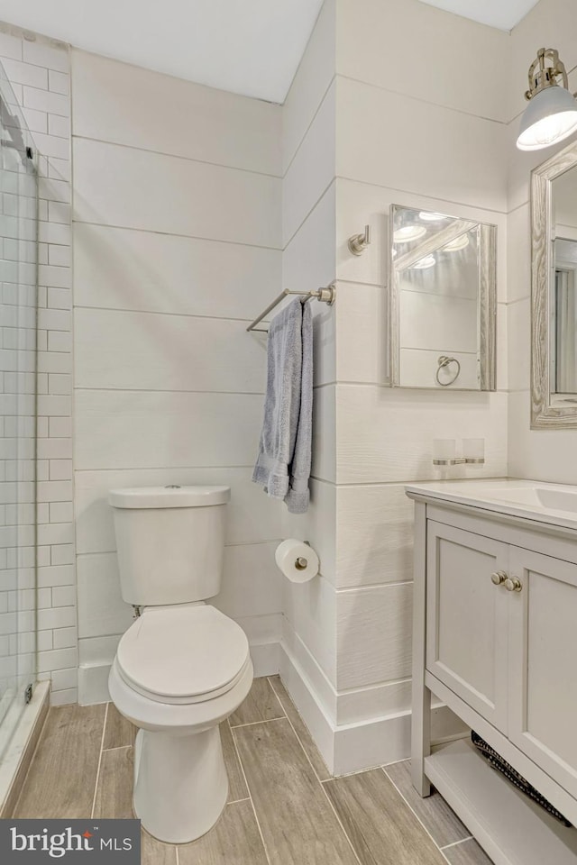 bathroom featuring a shower with door, toilet, and vanity