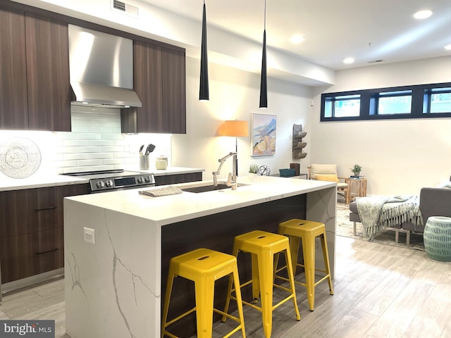 kitchen with wall chimney range hood, a kitchen breakfast bar, sink, and a center island with sink