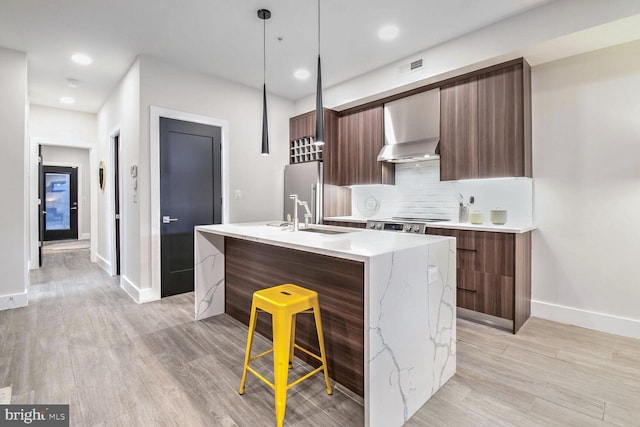 kitchen featuring sink, a kitchen island with sink, wall chimney range hood, and pendant lighting