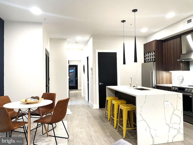 kitchen featuring range with electric cooktop, a breakfast bar, high end refrigerator, a kitchen island with sink, and dark brown cabinets