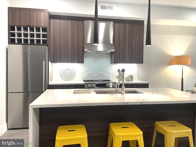 kitchen with stainless steel fridge, a kitchen breakfast bar, a center island with sink, and wall chimney range hood