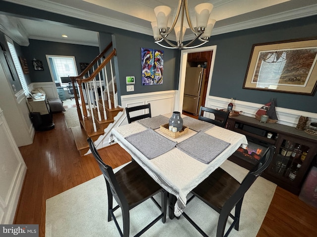 dining space with dark wood-type flooring, ornamental molding, and a chandelier