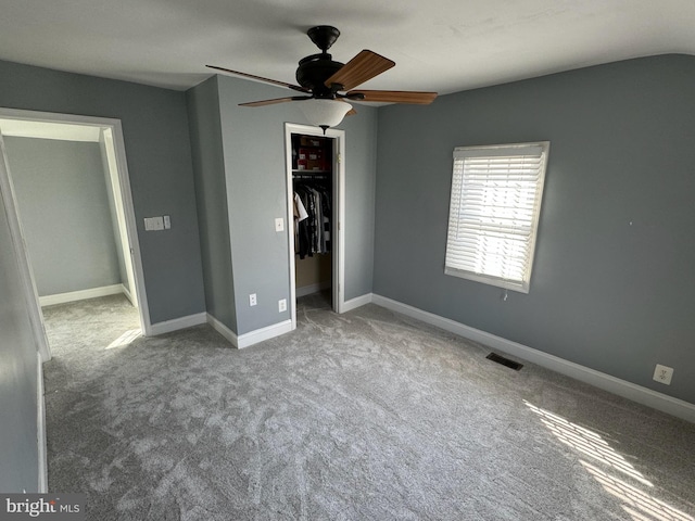 unfurnished bedroom featuring light carpet, a spacious closet, a closet, and ceiling fan