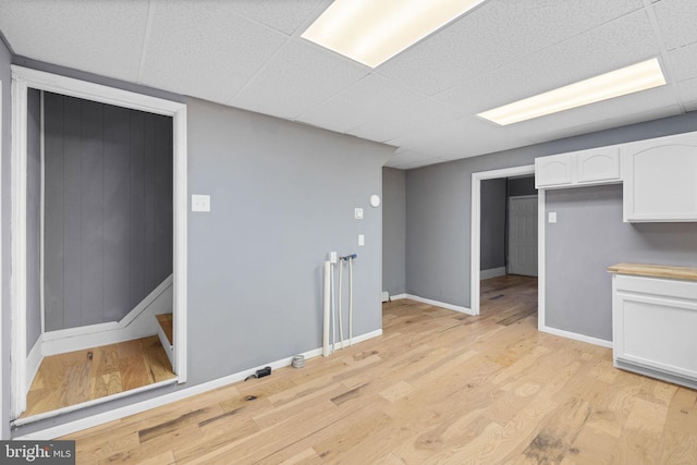 interior space featuring a paneled ceiling, white cabinetry, and light hardwood / wood-style flooring