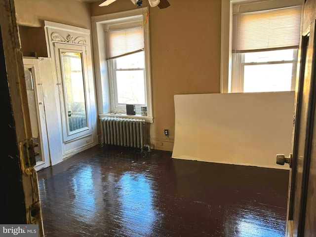 empty room featuring ceiling fan, radiator heating unit, and dark hardwood / wood-style flooring