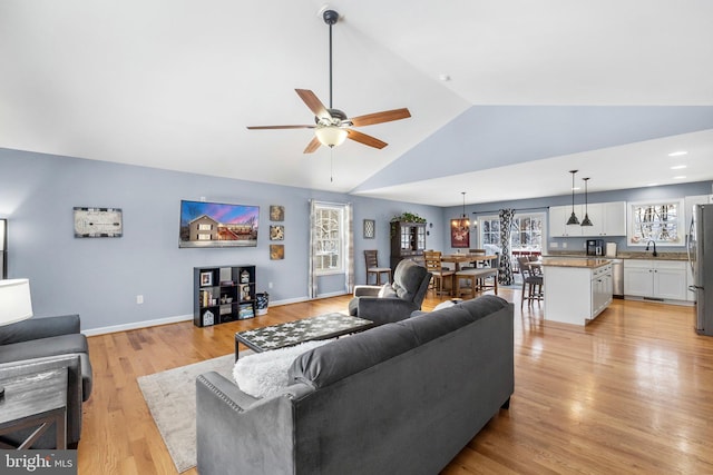 living room with light wood-type flooring, ceiling fan, vaulted ceiling, and sink