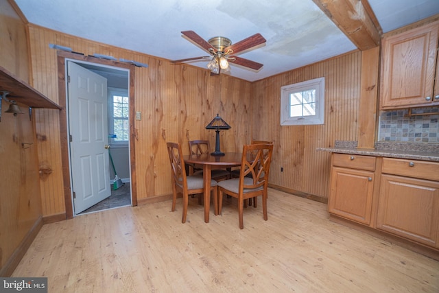 dining space with ceiling fan, light hardwood / wood-style flooring, wooden walls, and beamed ceiling