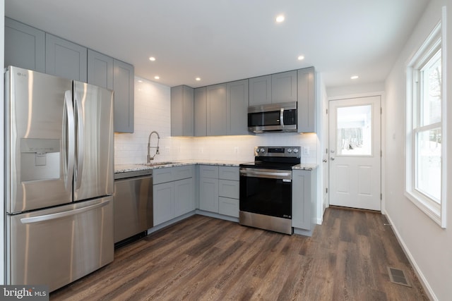 kitchen with sink, gray cabinetry, light stone counters, appliances with stainless steel finishes, and dark hardwood / wood-style flooring