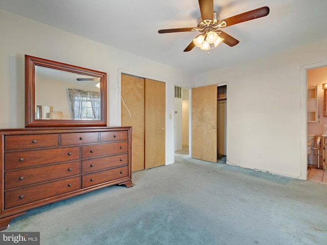 bedroom featuring ensuite bathroom, light colored carpet, ceiling fan, and two closets