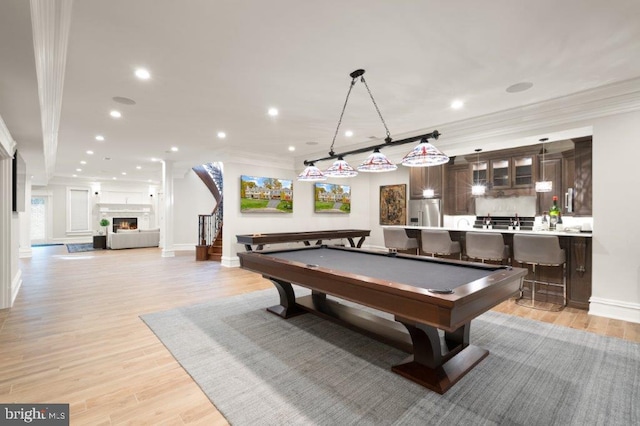 rec room with billiards, a large fireplace, light hardwood / wood-style flooring, bar, and ornamental molding