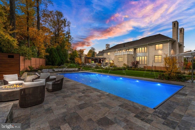 pool at dusk featuring pool water feature, an outdoor living space with a fire pit, and a patio area