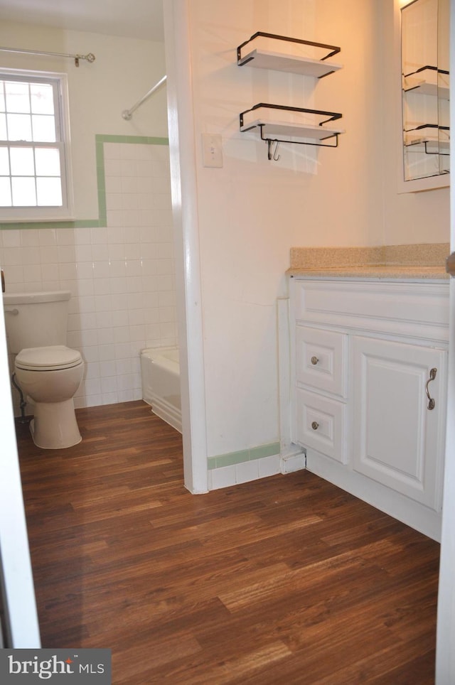 full bathroom with toilet, vanity, tile walls, washtub / shower combination, and hardwood / wood-style floors