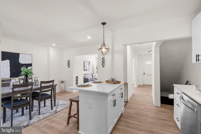 kitchen with decorative light fixtures, white cabinets, a kitchen bar, stainless steel dishwasher, and light hardwood / wood-style floors