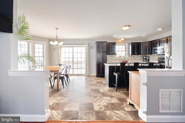 kitchen with a kitchen breakfast bar, dark brown cabinets, appliances with stainless steel finishes, decorative light fixtures, and decorative backsplash