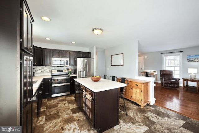 kitchen with dark brown cabinets, appliances with stainless steel finishes, backsplash, a center island, and a breakfast bar area