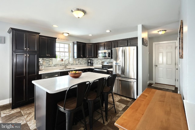 kitchen featuring appliances with stainless steel finishes, a center island, sink, backsplash, and a breakfast bar area