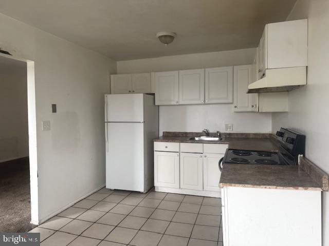 kitchen featuring electric stove, white fridge, sink, light tile patterned floors, and white cabinets