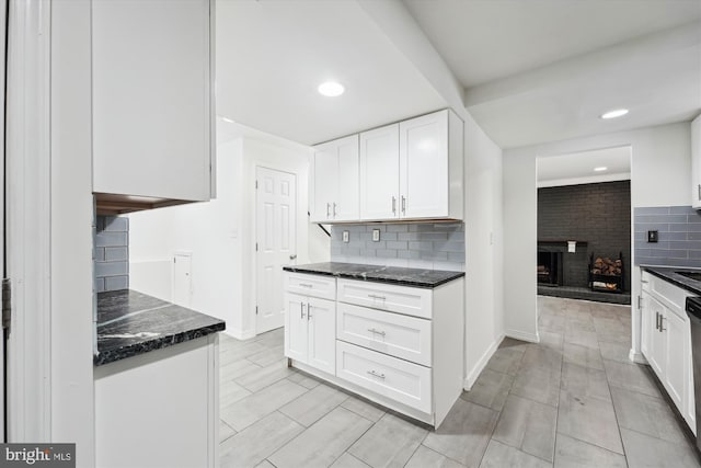 kitchen featuring a fireplace, white cabinetry, dishwasher, backsplash, and dark stone counters