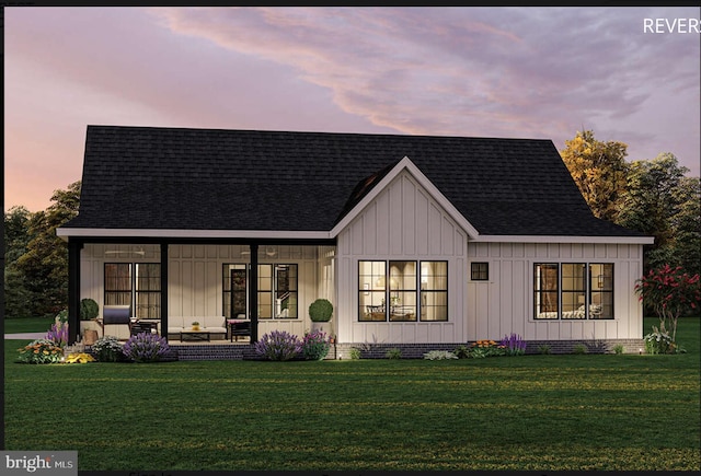 back house at dusk featuring a porch and a lawn