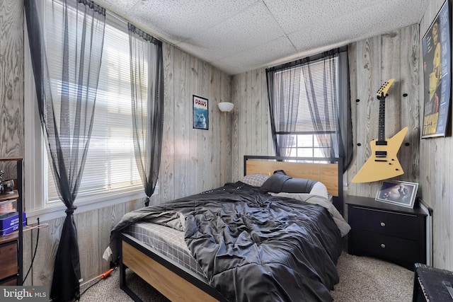 bedroom featuring a drop ceiling, wood walls, and carpet flooring