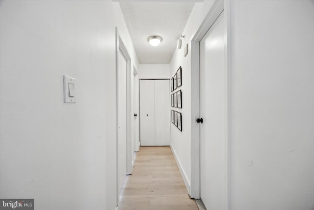 hallway with a textured ceiling and light hardwood / wood-style floors