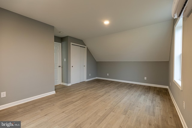 additional living space with lofted ceiling, a wall unit AC, and light wood-type flooring