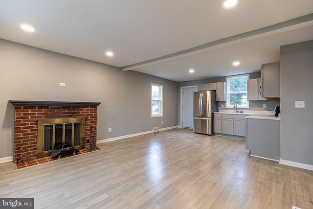 unfurnished living room featuring beam ceiling, sink, a fireplace, and light hardwood / wood-style flooring