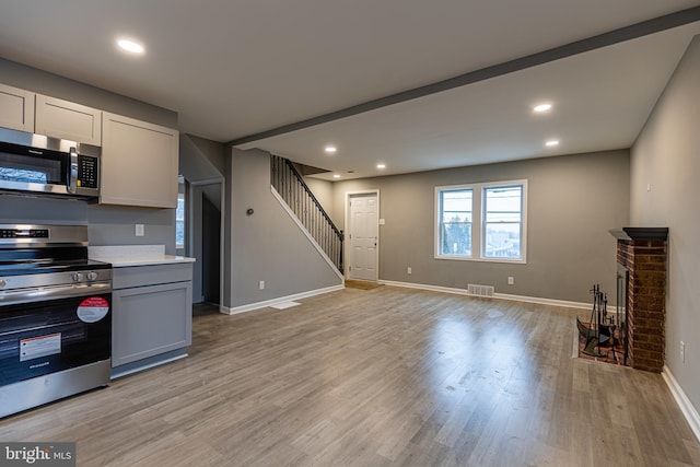 kitchen with light wood-type flooring, appliances with stainless steel finishes, gray cabinets, a fireplace, and white cabinets