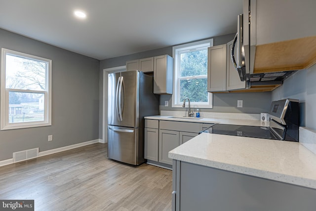 kitchen featuring gray cabinets, appliances with stainless steel finishes, sink, light stone counters, and light wood-type flooring