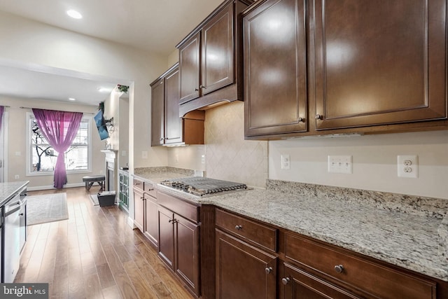 kitchen with light stone countertops, dark brown cabinetry, light hardwood / wood-style flooring, and stainless steel appliances